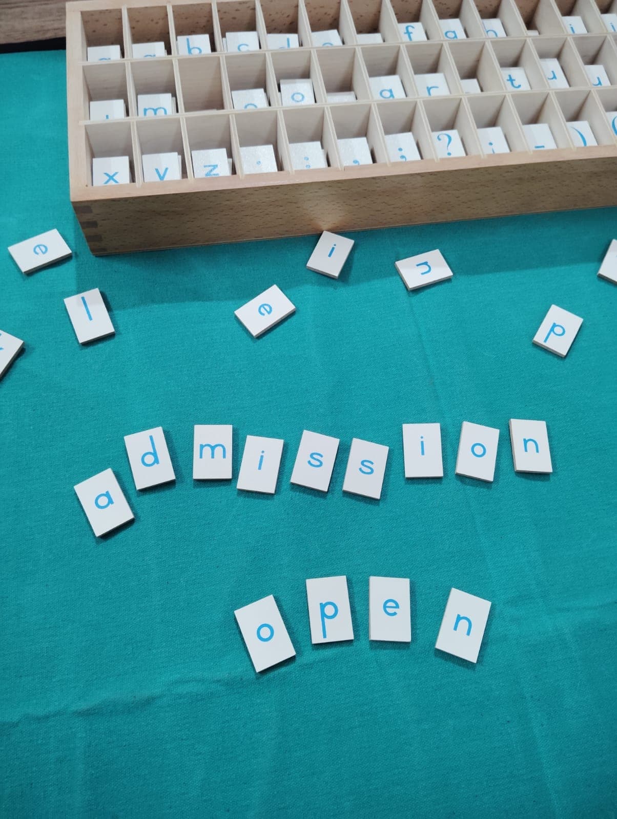 The word ‘admission open’ spelled out with Montessori letter tiles